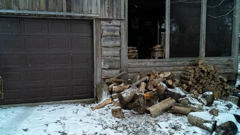 Chopped Firewood Pile with Axe by Rustic Wood Cottage Garage in Winter Snow 스톡 사진