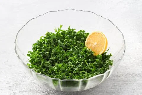 Chopped kale cabbage leaves mashed with lemon juice, half a lemon in a tran.. Foto stock