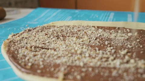 Chopped Nuts Being Sprinkled Over Chocolate Hazelnut Spread on Flat Raw Dough Stock Footage 334119799