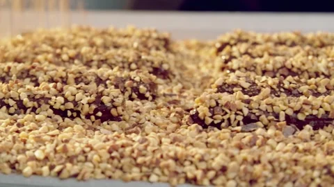 Chopped nuts cascade onto chocolate-coated confectionery during production Stock Footage 348703611