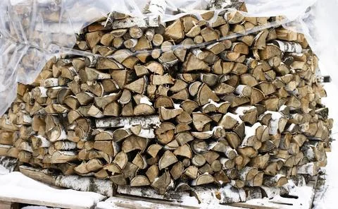 Chopped stack of firewood under snow. Preparation of firewood for the winter Stock Photos
