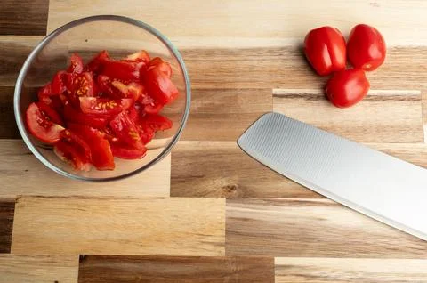 Chopped tomatoes in a bowl with knife and whole tomatoes Stock Photos