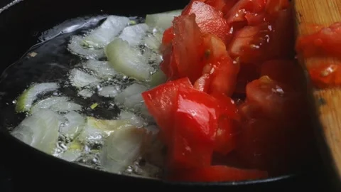 Chopped tomatoes fall into a frying pan with onions, mixed with a spatula. .. Stock Footage 297098623