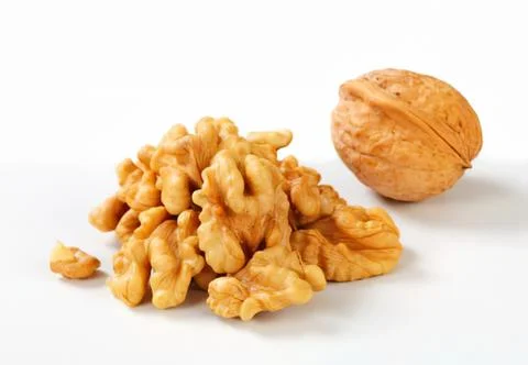 Chopped walnuts with whole walnut on plain surface Stock Photos