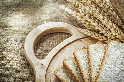 Chopping board sliced bread wheat ears on sacking background 스톡 사진