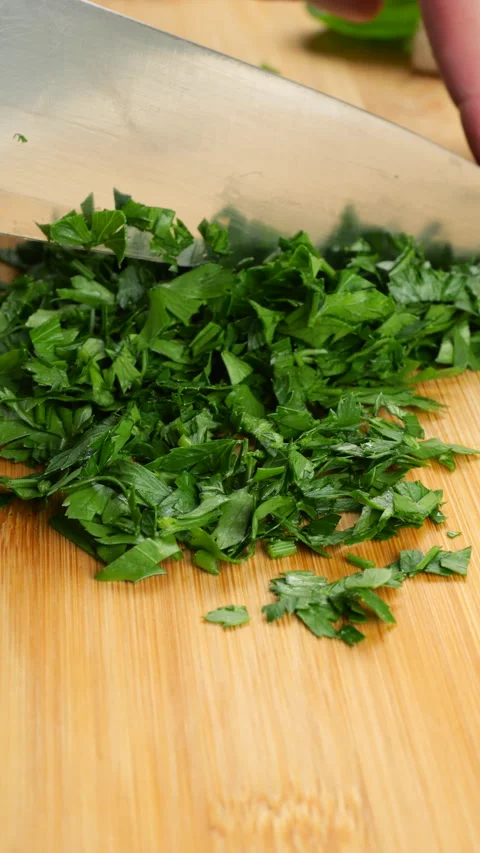 Chopping fresh green parsley with a sharp knife on a bamboo cutting board. 库存影片 341478575