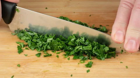 Chopping fresh green parsley with a sharp knife on a wooden cutting board. 库存影片 341478925