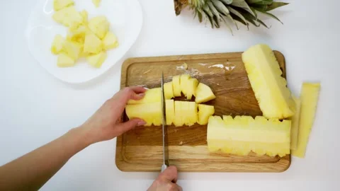 Chopping fresh pineapple into bite-sized pieces on wooden cutting board for.. 库存影片 337545178