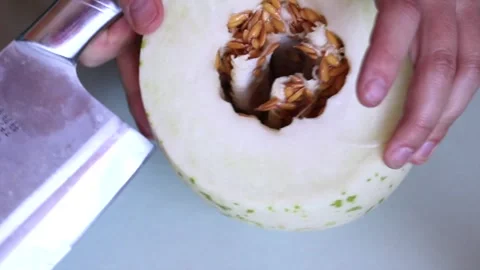 Chopping honey globe melon in half with large knife, showing seeds inside Stock Footage 174737548