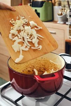 Chopping onions and adding them to a pot on the stove in a home kitchen setti Foto stock