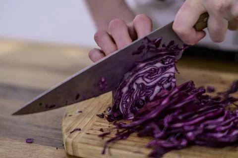 Chopping red cabbage with a kitchen knife on a wooden cutting board Stock Photos