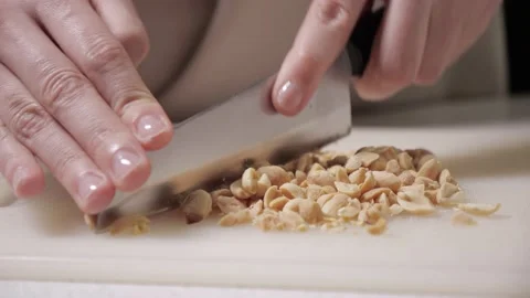 Chopping roasted peanuts with a knife. white cutting board. Stock Footage 218602096