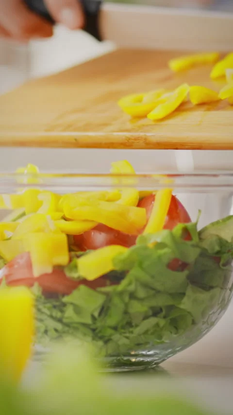 Chopping yellow peppers and preparing fresh salad ingredients in a bright ki Stock Footage 331537534