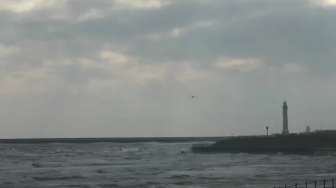 Choppy sea, waves lapping on shore with lighthouse and break water in winter Stock Footage 1097651
