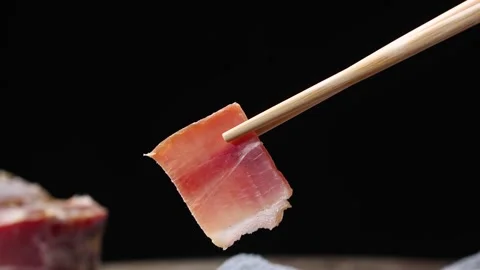 Chopsticks Holding Thin Slice of Cured Pork Belly on Dark Background Stock Footage 340455637