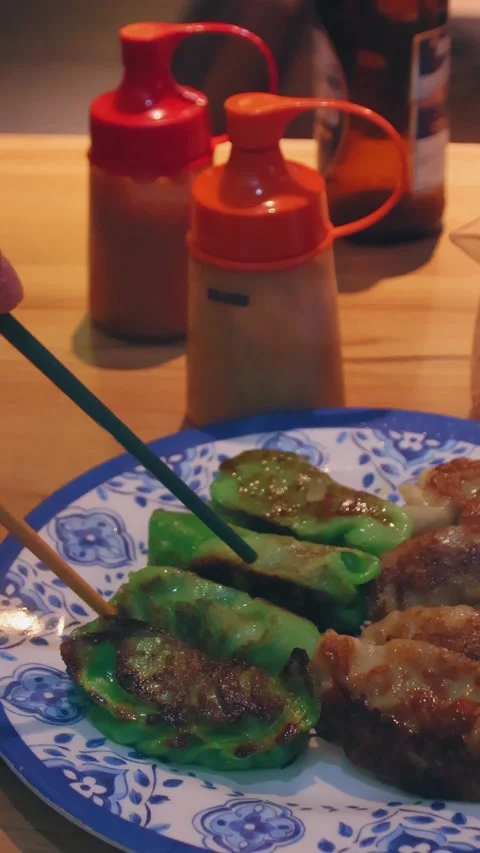 Chopsticks picking up fried green spinach momo or dumplings from a plate Stock Footage 332596931