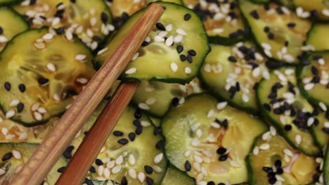 Chopsticks picking up a marinated cucumber slice with soy sauce and sesame seeds Stock Footage 314363957