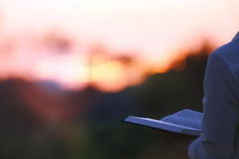 A Christian praying while looking at the setting sun and the holy bible Stock Photos