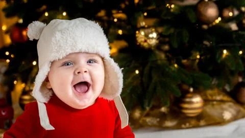 Christmas baby is smiling. A cute little girl in a red dress and white hat ex Stock Photos