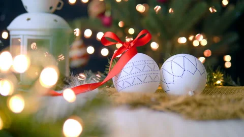 Christmas balls with red bow on table aganist blurred tree lights at home Stock Footage 140977228