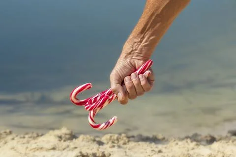 Christmas candy cane in hand.Candy cane in a human hand on the beach.The co.. Stock Photos