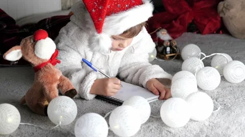 Christmas child in red hat writing letter about wishes to Santa Claus Stock Footage 167615917
