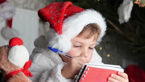 Christmas child in red hat writing letter about wishes to Santa Claus Stock Footage 167616151