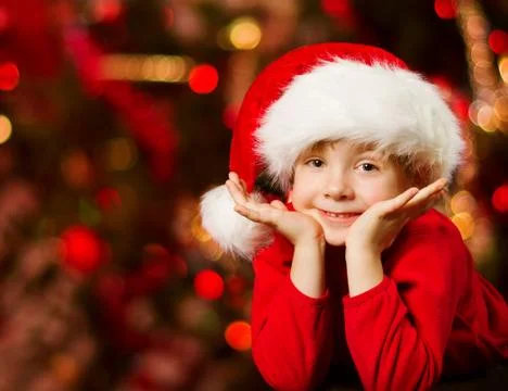 Christmas child in Santa hat smiling over red lights background Stock Photos
