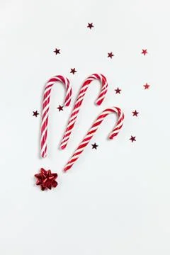 Christmas composition three caramel candy canes, confetti stars and red bow o Stock Photos