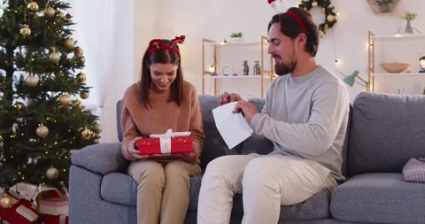 Christmas couple chatting on sofa, holding wrapped gift by decorated tree Stock Footage 320545796