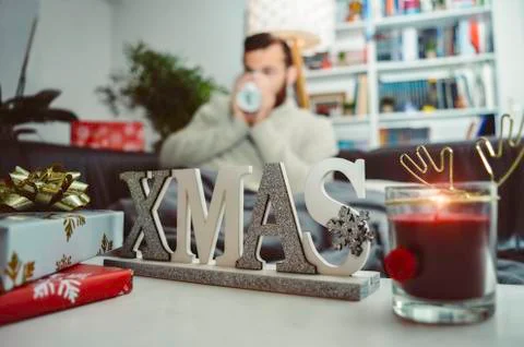 Christmas decorations gifts and candle with young man drinking hot drink Stock Photos