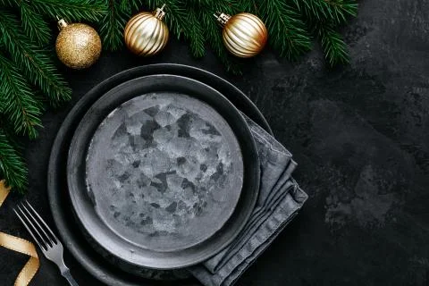 Christmas dinner background with empty plate and gold decor on dark table. Stock Photos