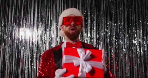 Christmas funny dance of Santa dancer with gift box in front of tinsel curtains Stock Footage 340354322