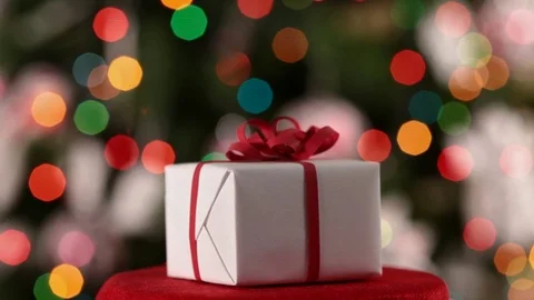 Christmas gift box spinning in front of decorated xmas tree Stock Footage