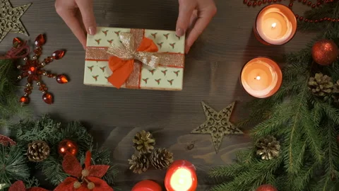 Christmas gift, top-down view. Female hands put a box with a gift on a wood Stock Footage 144468434