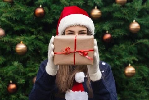 A Christmas gift. A young girl wearing a santa claus hat gives a gift made of Stock Photos