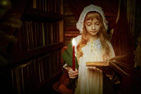 Christmas magic. Beautiful little girl in a nightgown reads a book holding a  Stock Photos