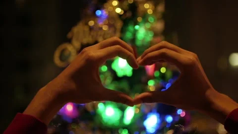 Christmas Night and hands making heart symbol in front of a Christmas tree Stock Footage 239020257