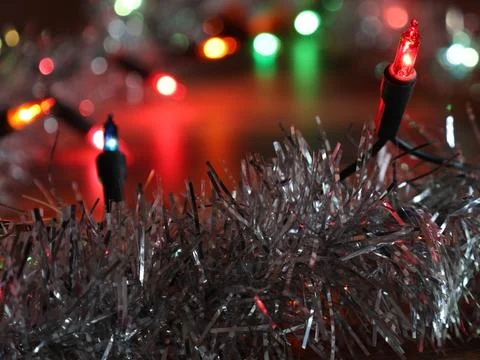 Christmas string lights illuminating silver tinsel decoration Stock Photos