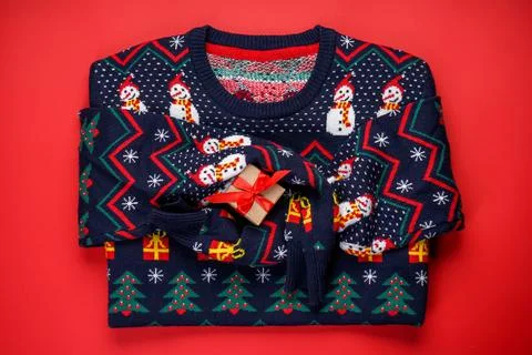 Christmas sweater with a pattern on a red background with a gift, top view Stock Photos