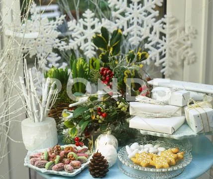 A Christmas Table Laid With Flowers, Presents, Candles And Biscuits In Front Of