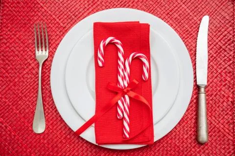 Christmas table setting. Candy canes on white plates and cutlery, red mat, to Stock Photos