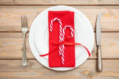 Christmas table setting. Candy canes on white plates and cutlery, wooden back Stock Photos