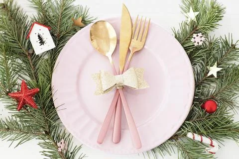 Christmas table setting . pink plate, cutlery with gold bow, fir branches, sn Stock Photos