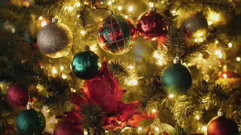 A Christmas tree adorned with bright, multicolored baubles, red flowers, and Stock Footage 280463745