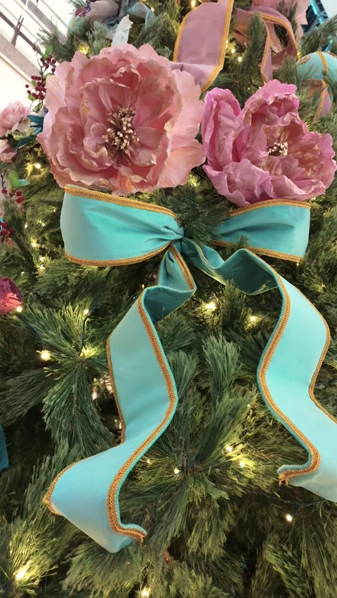 Christmas tree adorned with soft pink roses, and a bold turquoise ribbon bow. 動画素材 323487050
