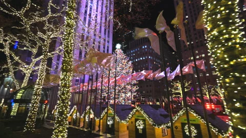 Christmas Tree glows beyond shaking flags in Rockefeller Center in NYC Stock Footage 226685370