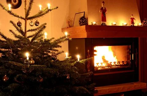 Christmas tree with lighted decorations next to burning fire in domestic home Stock Photos