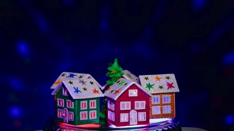 Christmas tree rotates on a stand surrounded by multi-colored Christmas houses Stock Footage 290371627