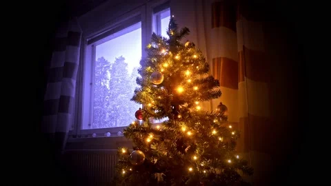 Christmas tree shining with orange color inside while it's snowing outside Stock Footage